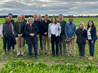 People gathered on a grassy field under a cloudy sky. People in the photo from left to right, are Md Ashrafuzzaman, Jamie Smith, Matt Lowe, Greg Jarman, Minister Gayle Tierney, Joe Jacobs, Greg Mason, Kevin Smith, Simone Warner, James Mann, Chinthaka Jayasinghe, Penny Riffkin, and Dilnee Suraweera.